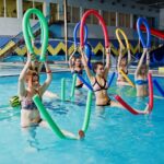 Fitness group of girls doing aerobical excercises in swimming pool at aqua park. Sport and leisure activities.